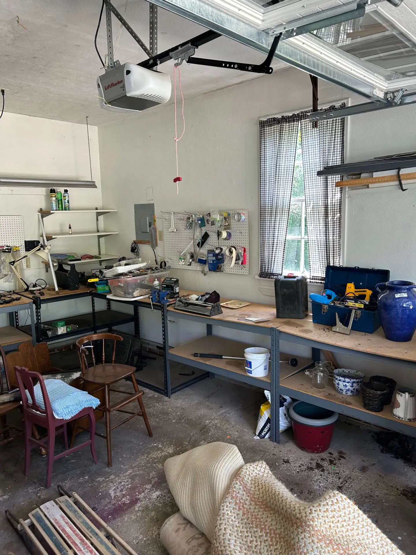 A cluttered residential garage with workbenches covered in tools, chairs, and everyday junk prior to a cleanout service in Bay Village, OH.