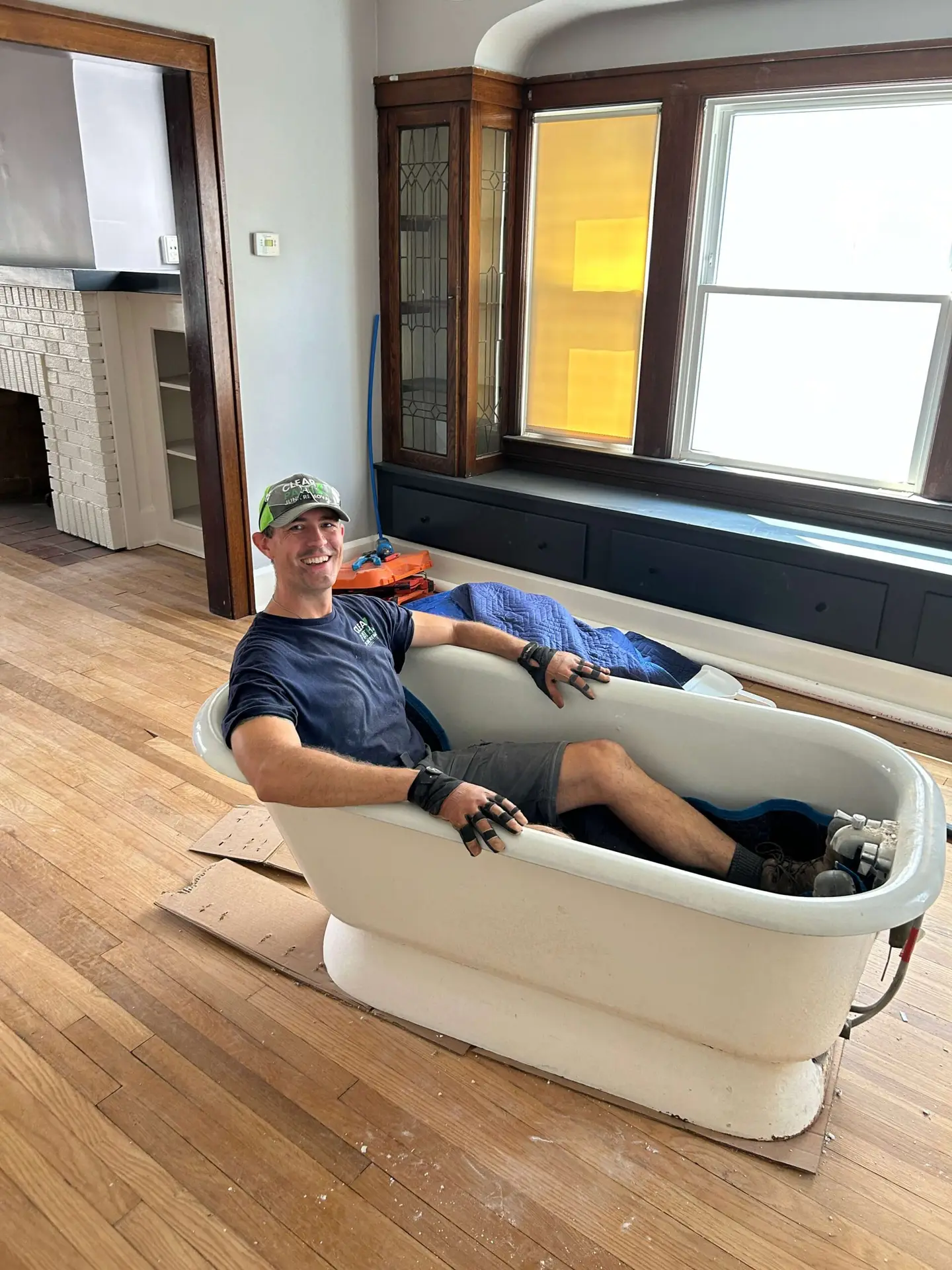 Clear Path Junk Removal team member sitting inside a heavy cast iron clawfoot tub during a century home interior cleanout in Lakewood, Ohio.