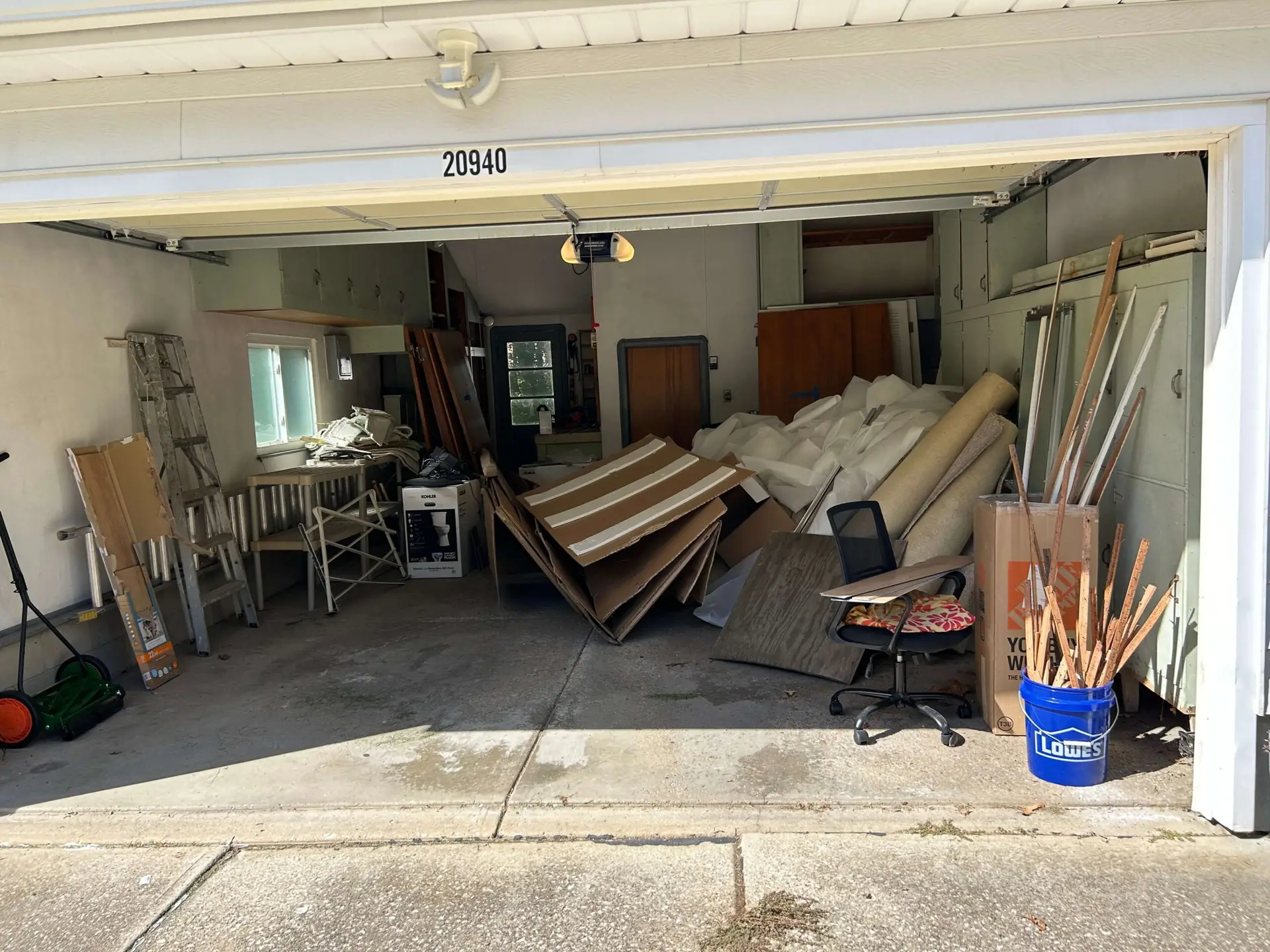 A cluttered residential garage filled with broken down cardboard, old furniture, and household debris prior to a same-day cleanout in Fairview Park, Ohio.